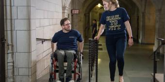 a man in a wheelchair with a woman walking next to him in the cathedral of learning