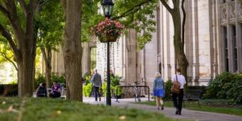 people walking on the sidewalk near the cathedral of learning