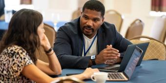 a man and a woman talking with two laptops on a table between them