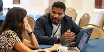 a man and a woman talking with two laptops on a table between them