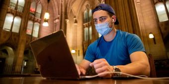 a man sitting at a table in the cathedral of learning commons room, looking at his laptop