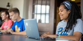 a woman smiling looking at a computer with two men in the background